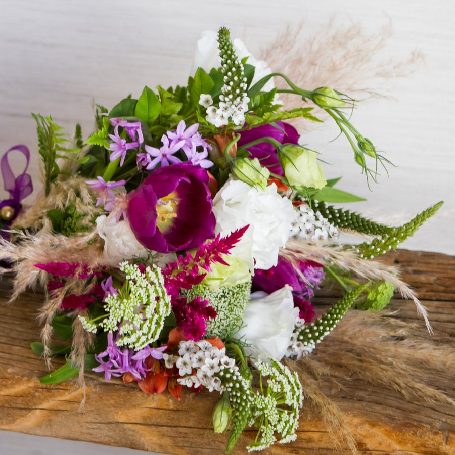 Bridal bouquet of magenta tulips, white roses and pampas on a wooden bench