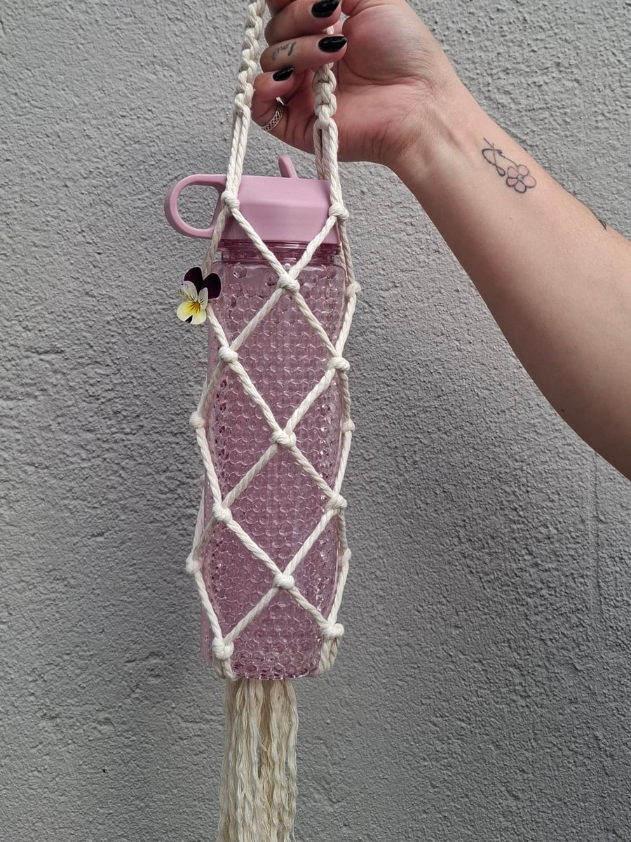 Cream macramé bottle carrier with a knotted handle and tassel