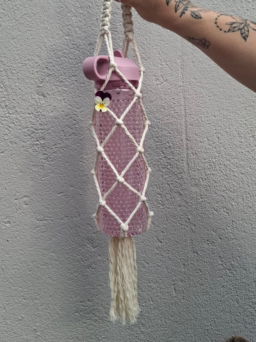 Pink bottle in a cream macramé carrier with a long tassel