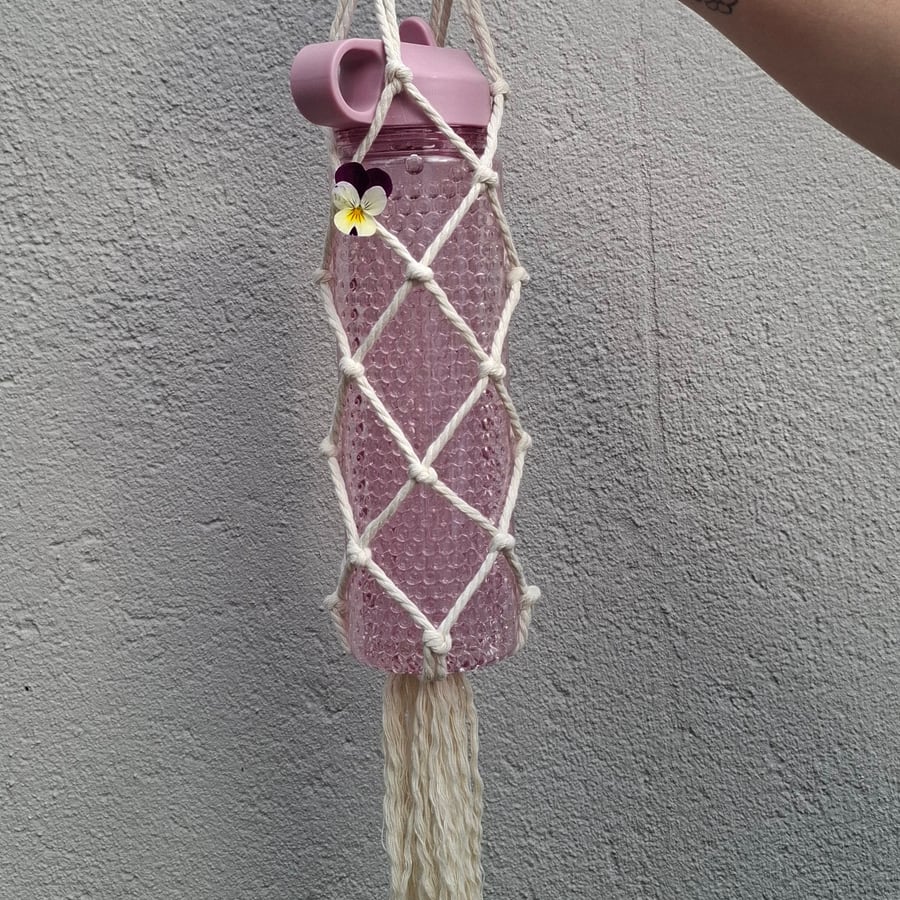 Pink bottle in a cream macramé carrier with a long tassel