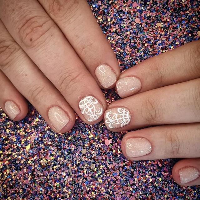 Nude nails with white lace detail on a glitter background